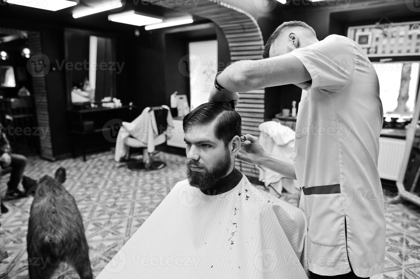 jovem barbudo cortando o cabelo pelo cabeleireiro enquanto está sentado na cadeira na barbearia. alma de barbeiro. foto