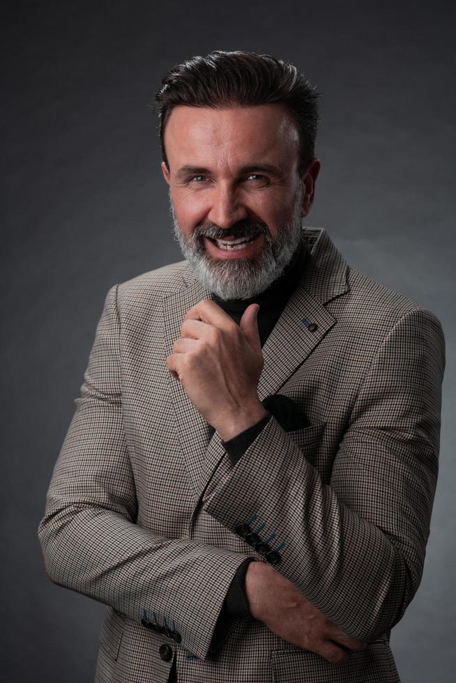 retrato de um elegante elegante empresário sênior com barba e roupas de negócios casuais em estúdio fotográfico isolado em fundo escuro, gesticulando com as mãos foto