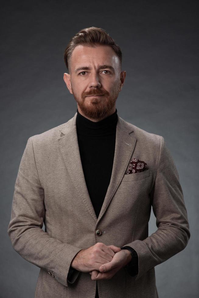 retrato de um elegante elegante empresário sênior com barba e roupas de negócios casuais em estúdio fotográfico isolado em fundo escuro, gesticulando com as mãos foto