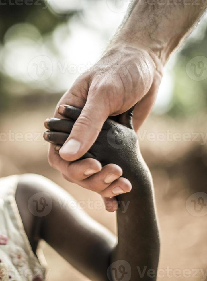 mão de criança africana, segurando uma mão branca de adultos foto