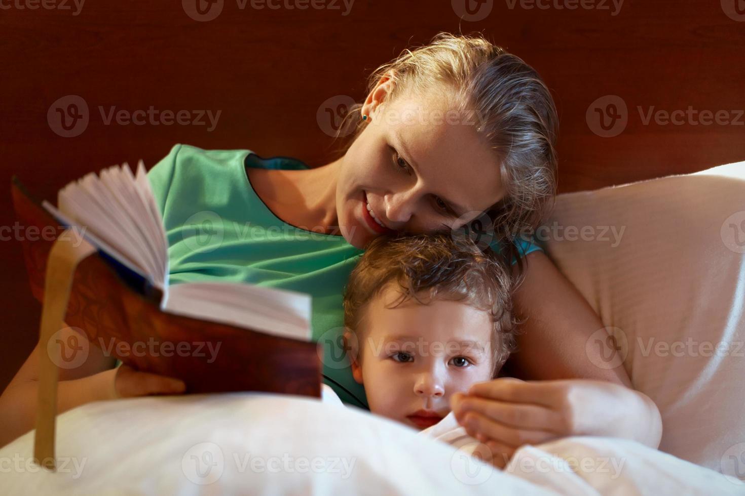 jovem mãe lendo para o filho na cama foto