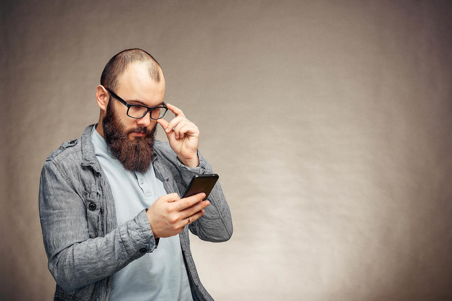 homem barbudo com óculos lendo más notícias no celular foto