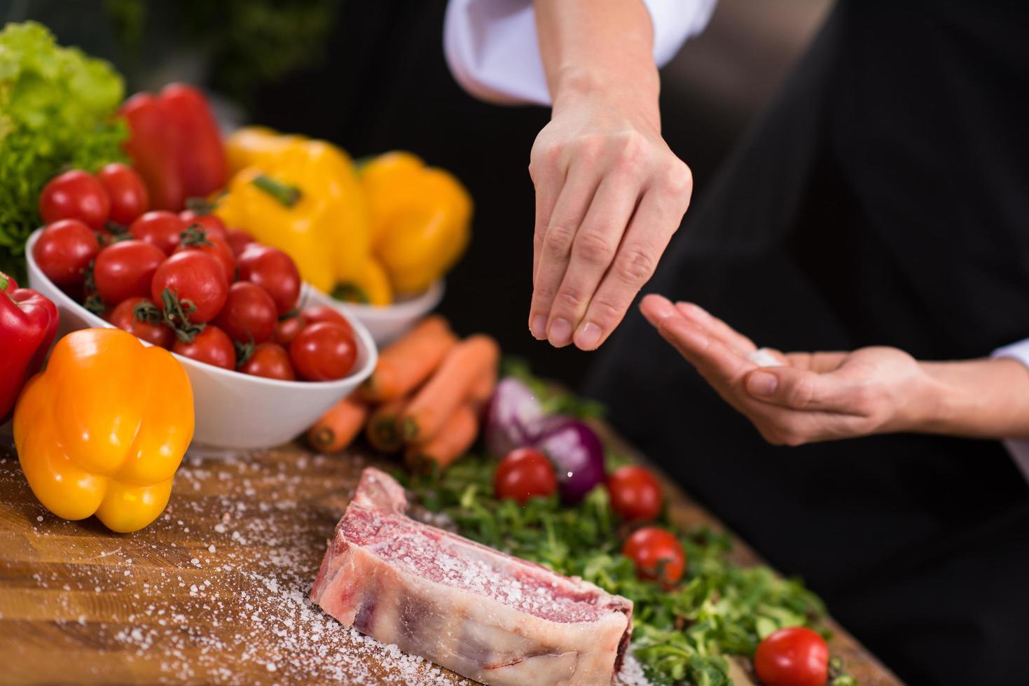 chef colocando sal na suculenta fatia de bife cru foto