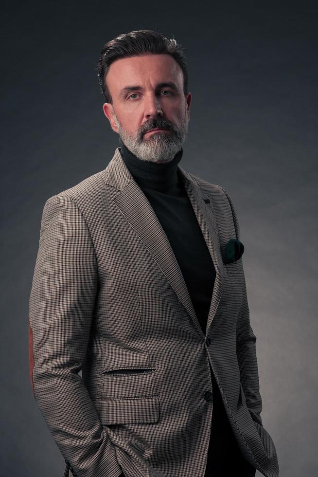 retrato de um elegante elegante empresário sênior com barba e roupas de negócios casuais em estúdio fotográfico isolado em fundo escuro, gesticulando com as mãos foto