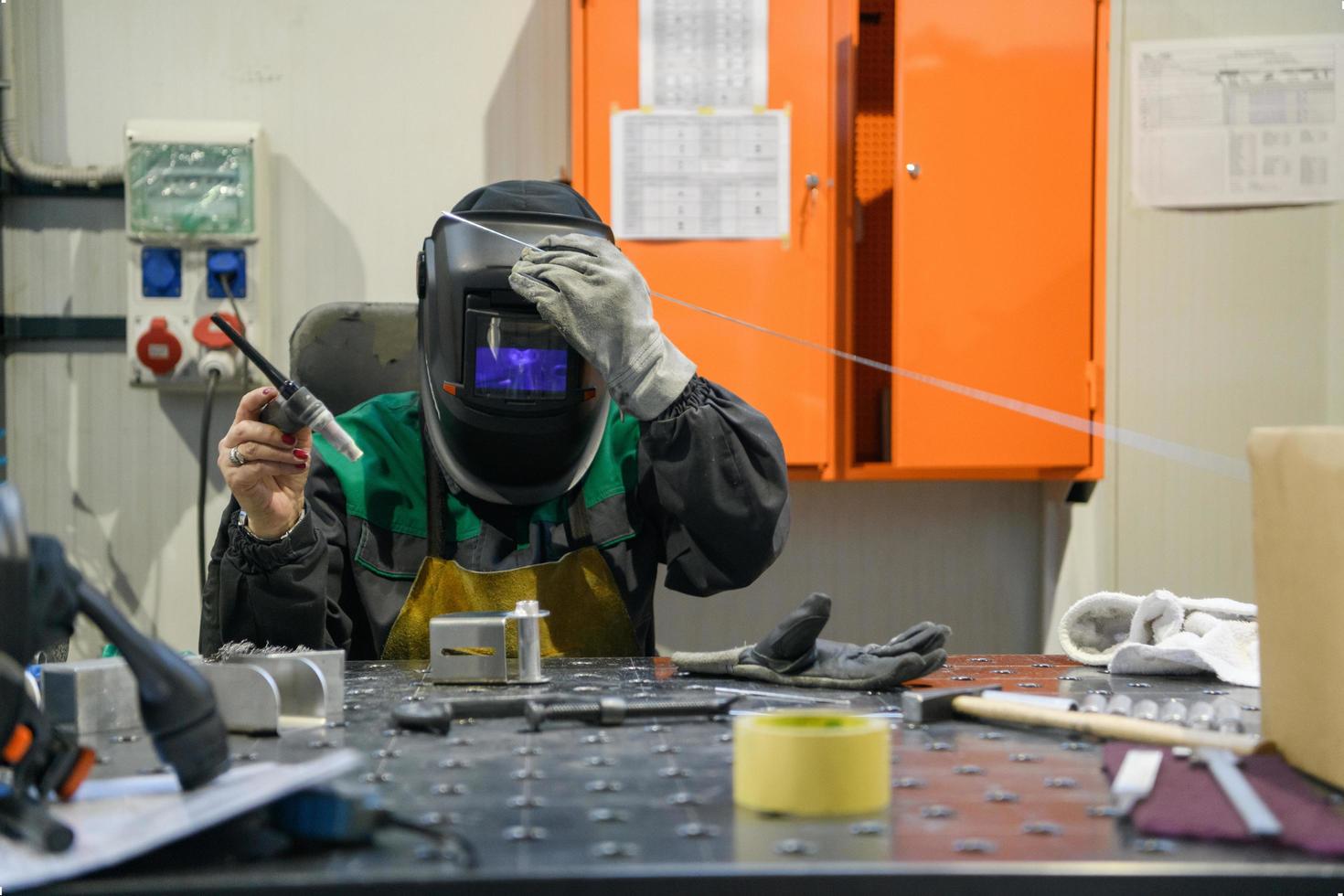 uma mulher empregada em uma fábrica moderna para a produção e processamento de metais em um trabalho uniforme de soldagem de materiais metálicos foto
