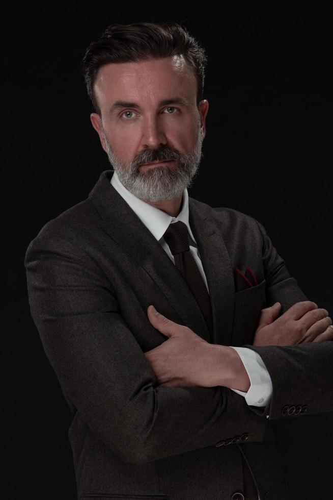 retrato de um elegante elegante empresário sênior com barba e roupas de negócios casuais em estúdio fotográfico isolado em fundo escuro, gesticulando com as mãos foto
