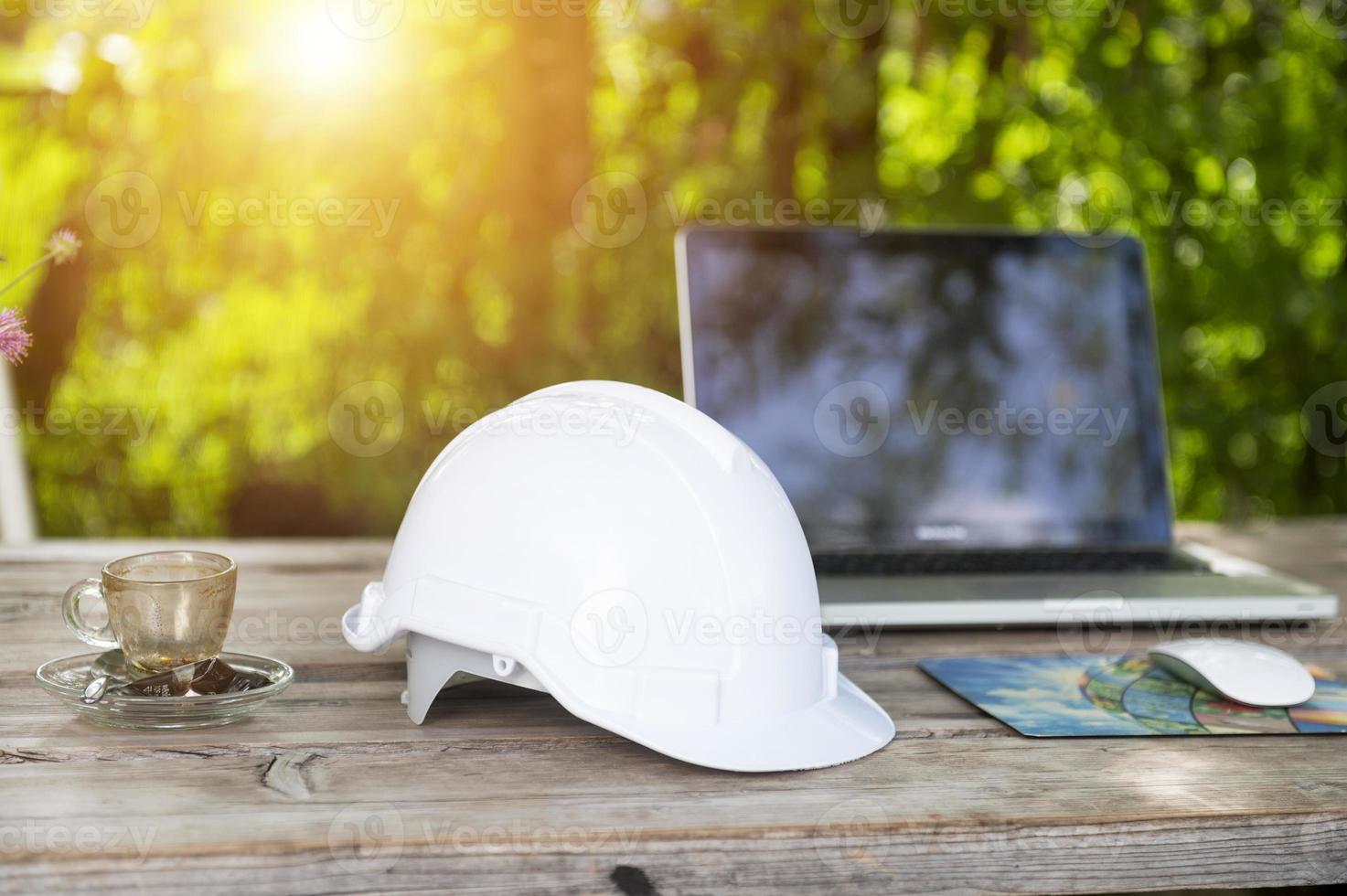 capacete branco e computador no café com fundo de luz solar, vista de engenheiro sentado planejamento de construção foto