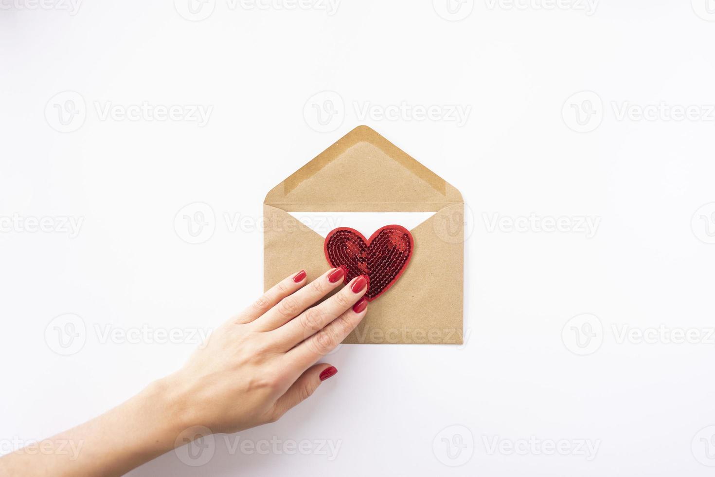 a mão de uma mulher segura um coração vermelho em um envelope marrom para dia dos namorados foto