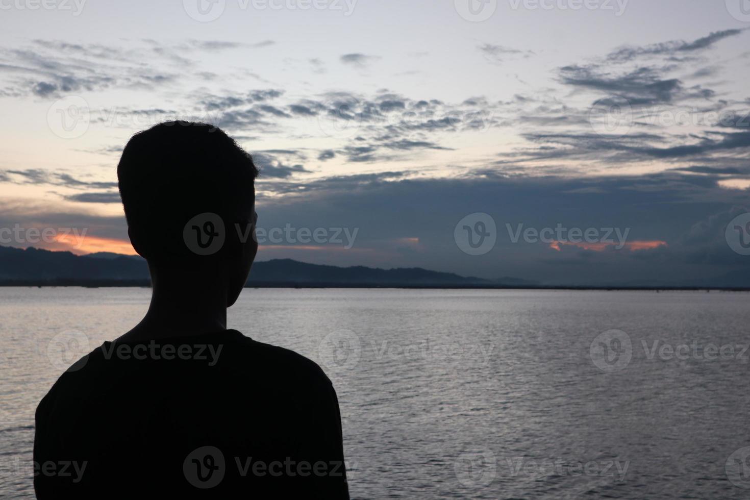 silhueta de um jovem de pé à beira do lago apreciando o pôr do sol. ambiente tranquilo na natureza foto