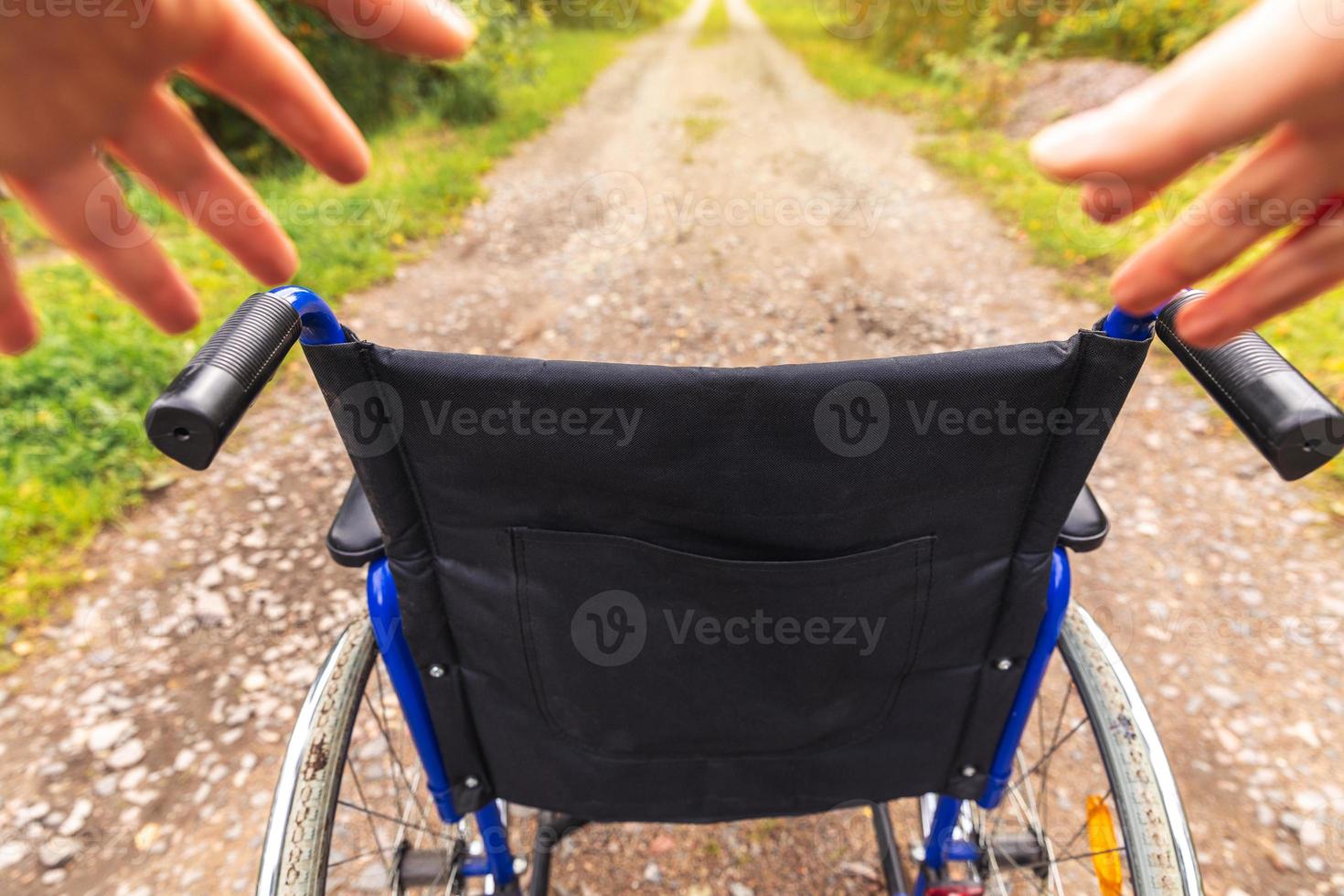 mãos segurando uma cadeira de rodas vazia no parque hospitalar à espera de serviços ao paciente. cadeira de rodas para pessoa com deficiência estacionada ao ar livre. acessível para pessoa com deficiência. conceito médico de cuidados de saúde. foto