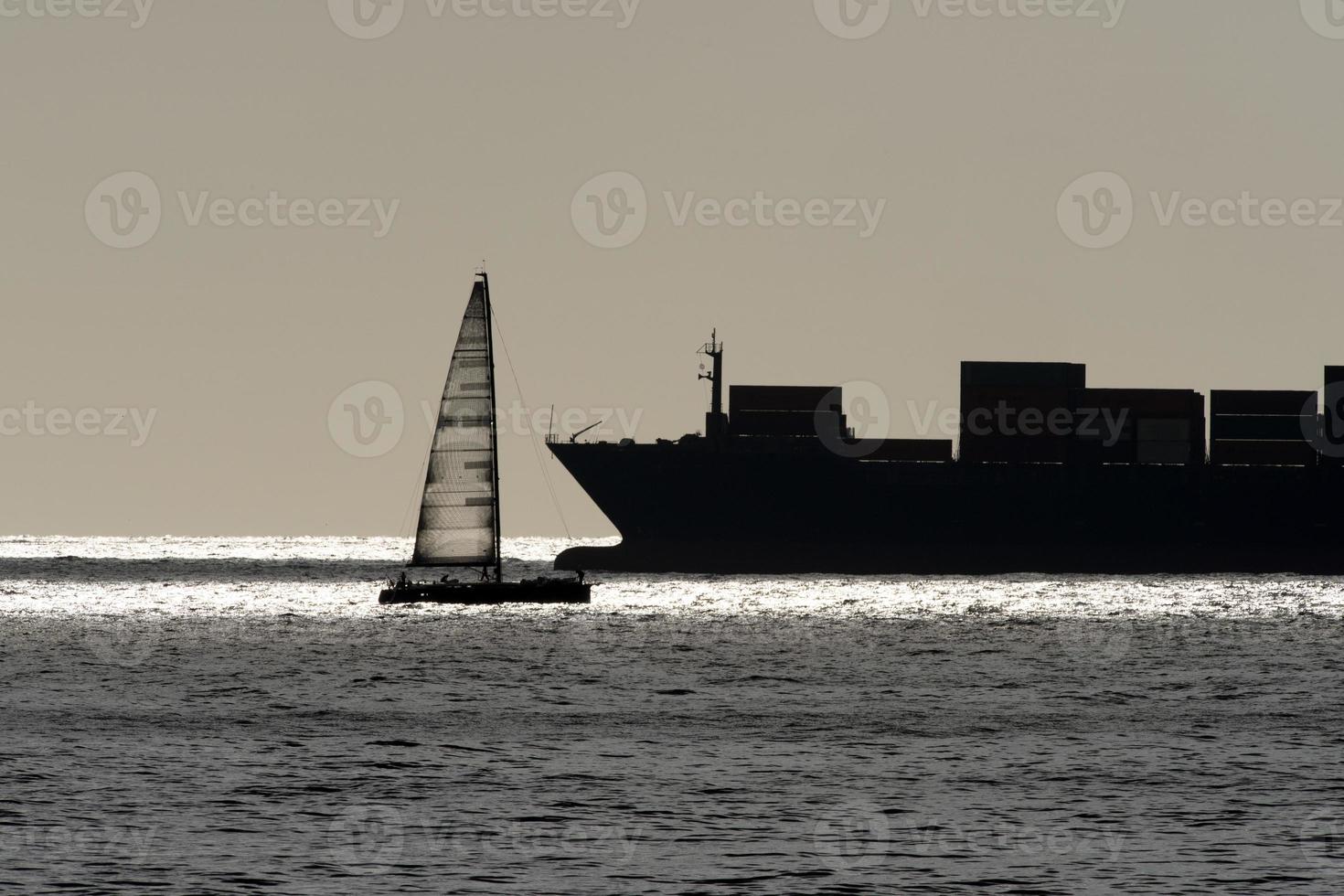 barco a vela e grande silhueta de navio porta-contentores foto