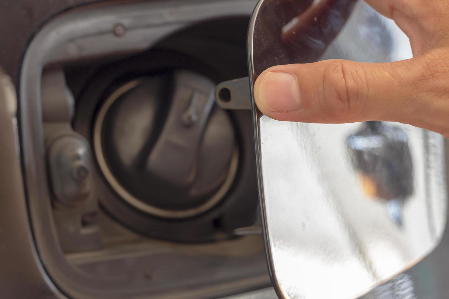close-up de uma mão abrindo a porta do tanque de combustível no carro foto