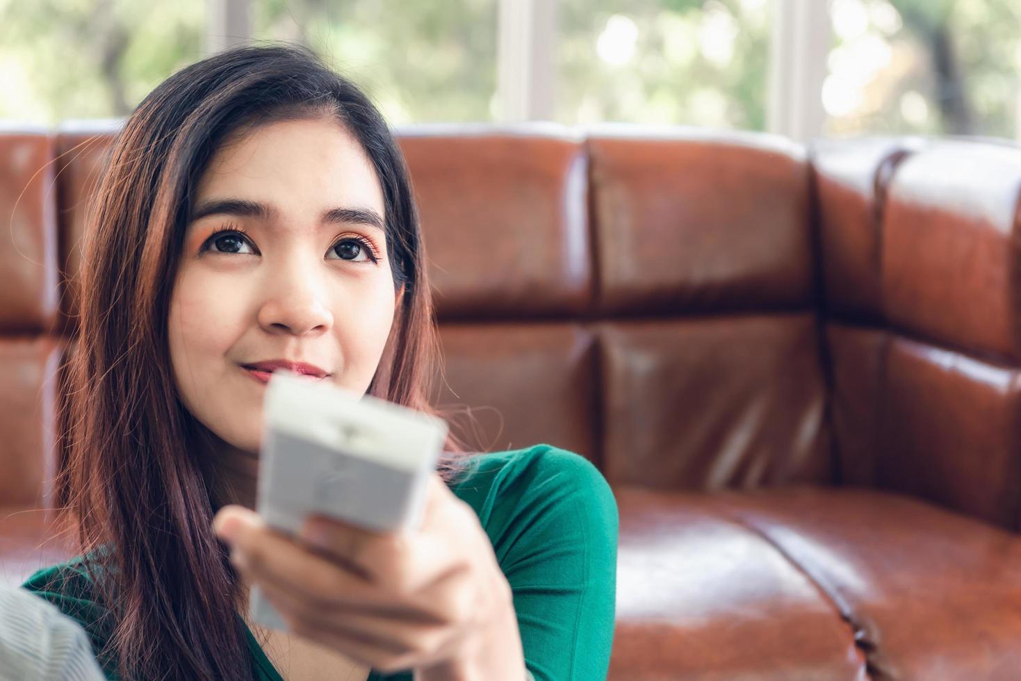 jovem mulher asiática, vista em casa, controlando o ar condicionado elétrico foto