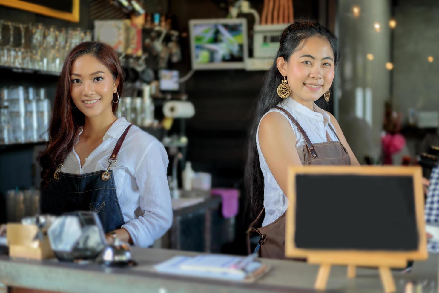 baristas asiáticos femininos sorrindo atrás do balcão da loja de café foto