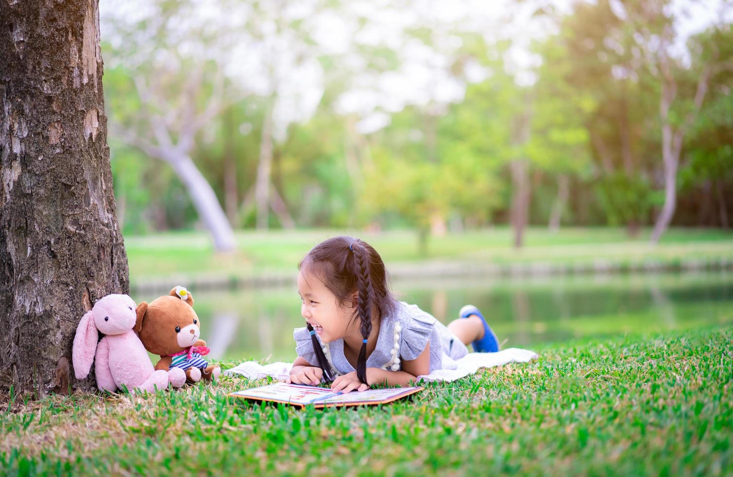 jovem menina asiática com livro e bichos de pelúcia no parque foto