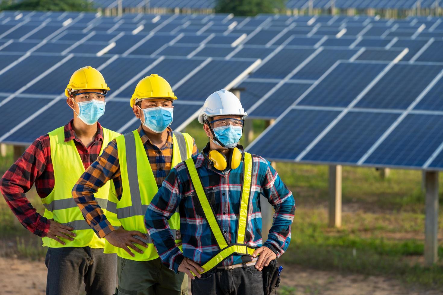 trabalhadores mascarados ao lado de painéis solares foto