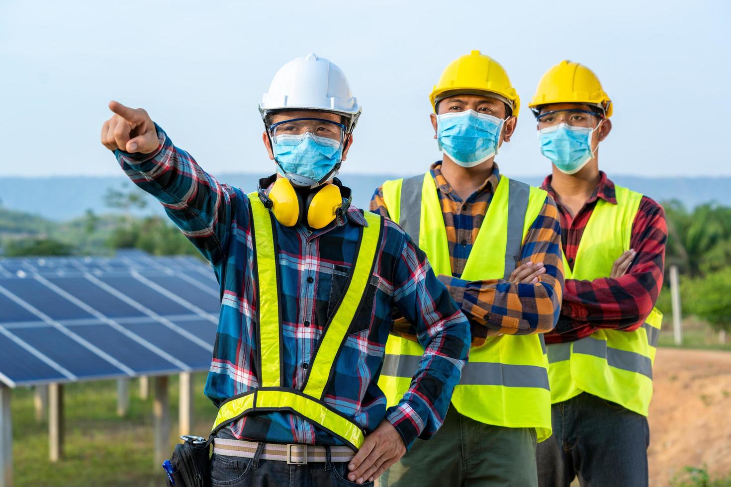 trabalhadores mascarados ao lado do painel solar foto