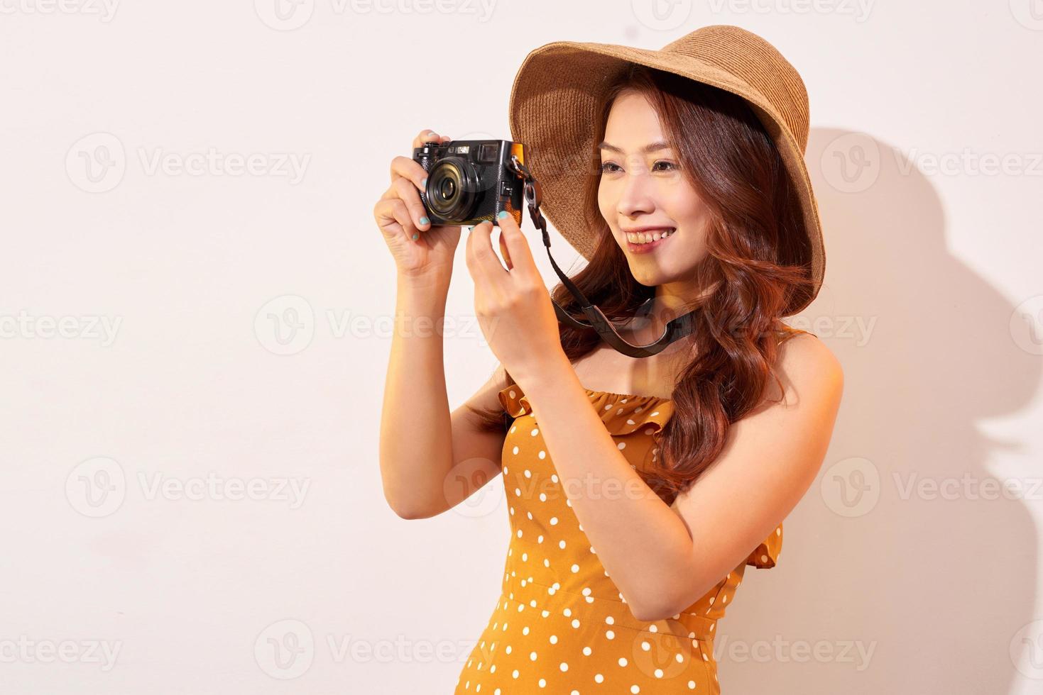 mulher jovem e atraente com uma câmera fotográfica na mão em um fundo bege isolado. o conceito de viagem foto