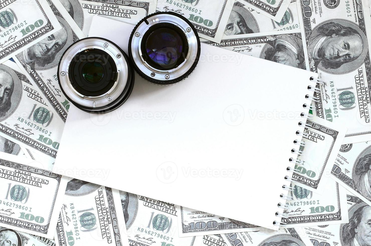 duas lentes fotográficas e um caderno branco estão no fundo de muitas notas de dólar. espaço para texto foto