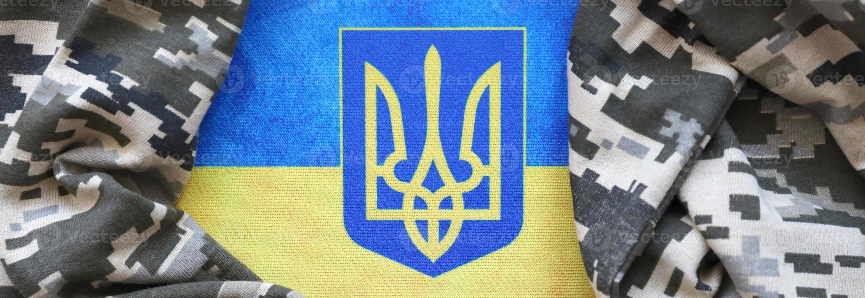 bandeira ucraniana e brasão com tecido com textura de camuflagem pixelizada. pano com padrão de camuflagem em formas de pixel cinza, marrom e verde com sinal de tridente ucraniano foto