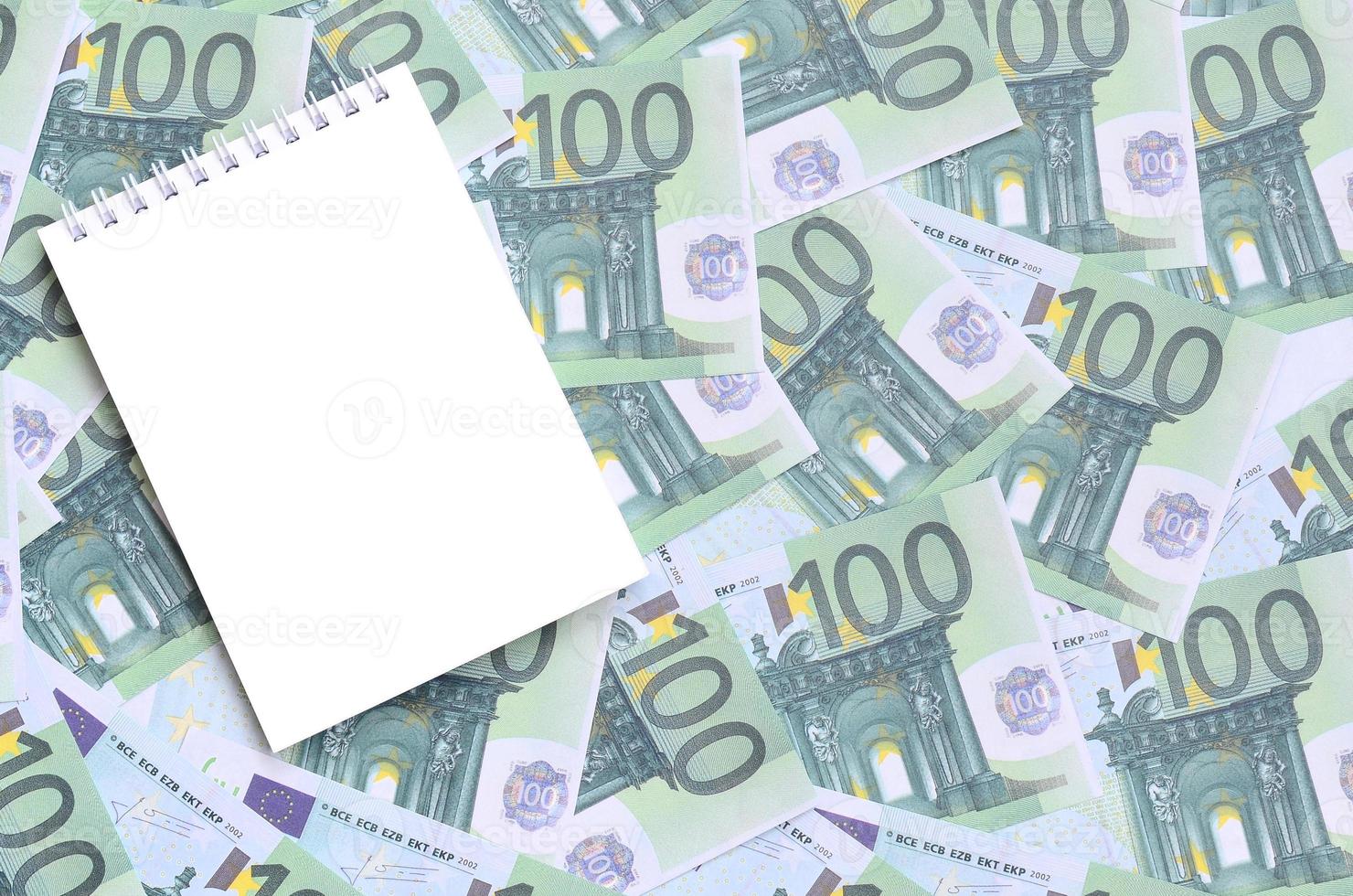 caderno branco com páginas limpas sobre um conjunto de denominações monetárias verdes de 100 euros. muito dinheiro forma uma pilha infinita foto