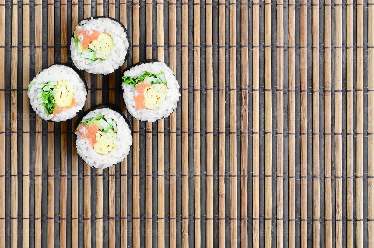 rolos de sushi encontra-se em uma esteira de serragem de palha de bambu. comida asiática tradicional. vista do topo. minimalismo plano leigo com espaço de cópia foto