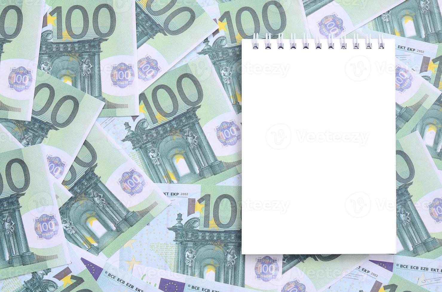 caderno branco com páginas limpas sobre um conjunto de denominações monetárias verdes de 100 euros. muito dinheiro forma uma pilha infinita foto