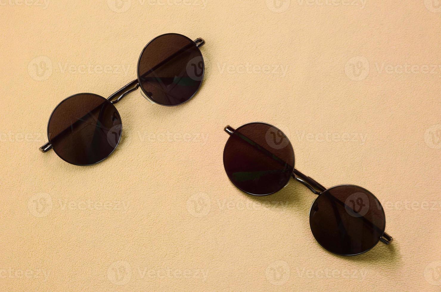dois elegantes óculos de sol pretos com óculos redondos estão em um cobertor feito de tecido de lã laranja claro macio e fofo. imagem de fundo na moda em cores da moda foto