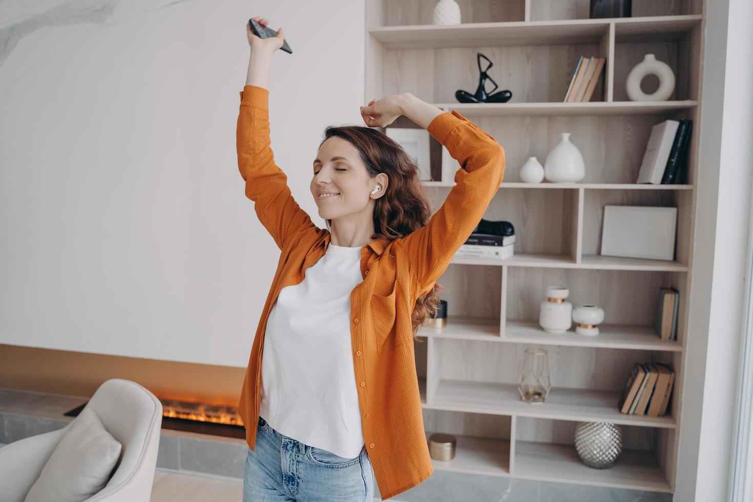 garota dança segurando o telefone ouve playlist musical curtindo o som em casa. anúncio de aplicativos de música foto