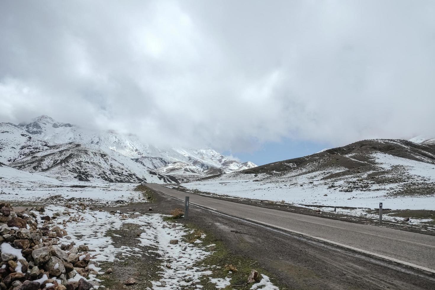 uma estrada pavimentada vazia cercada por montanhas cobertas de neve com céu nublado na faixa do alto atlas. Marrocos. foto