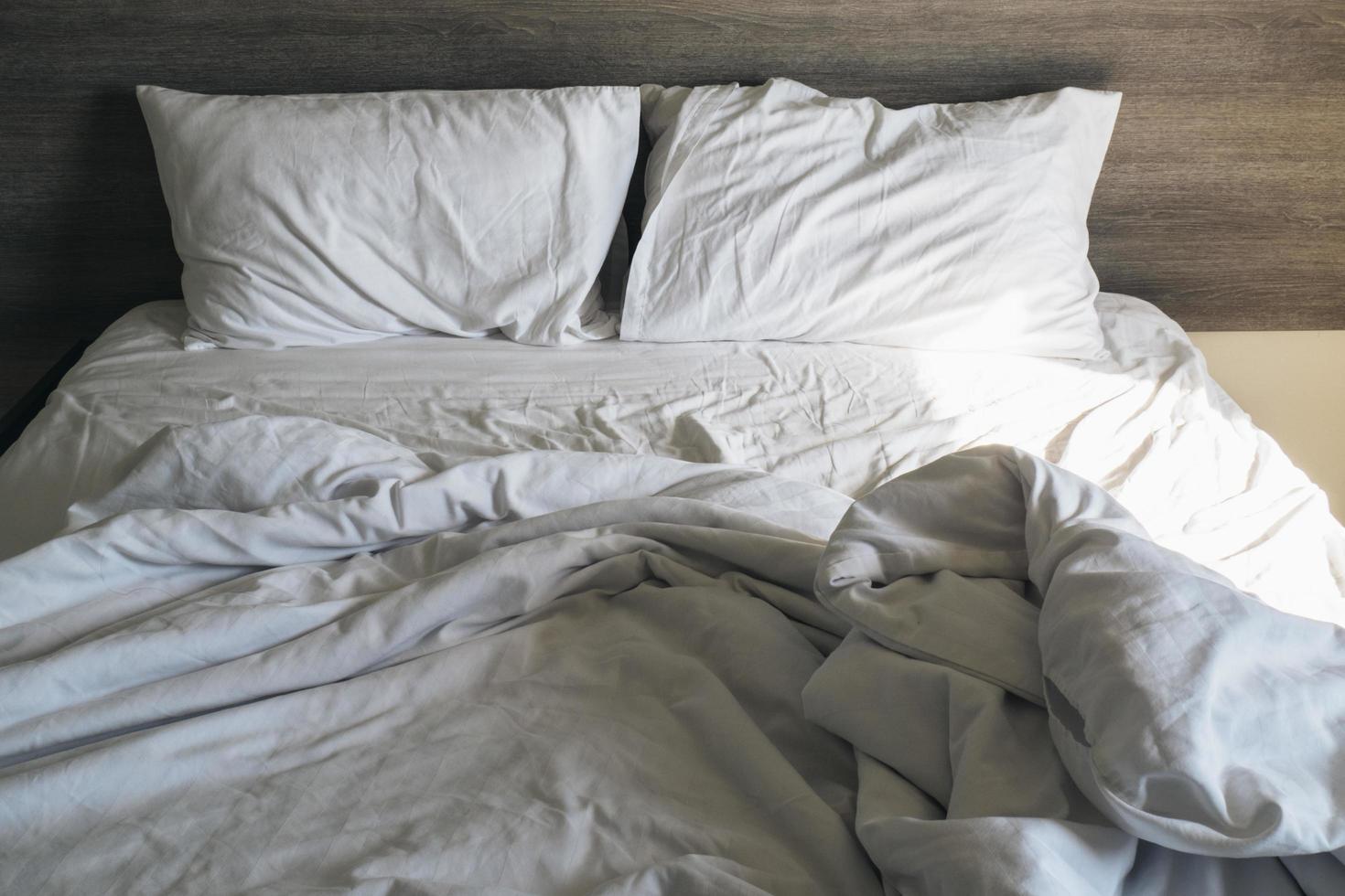 cama desfeita com edredom cinza e lençóis brancos foto