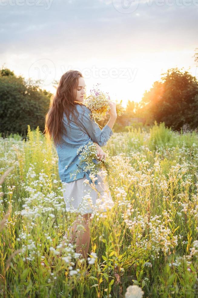 linda garota andando no campo no verão com flores silvestres. foto