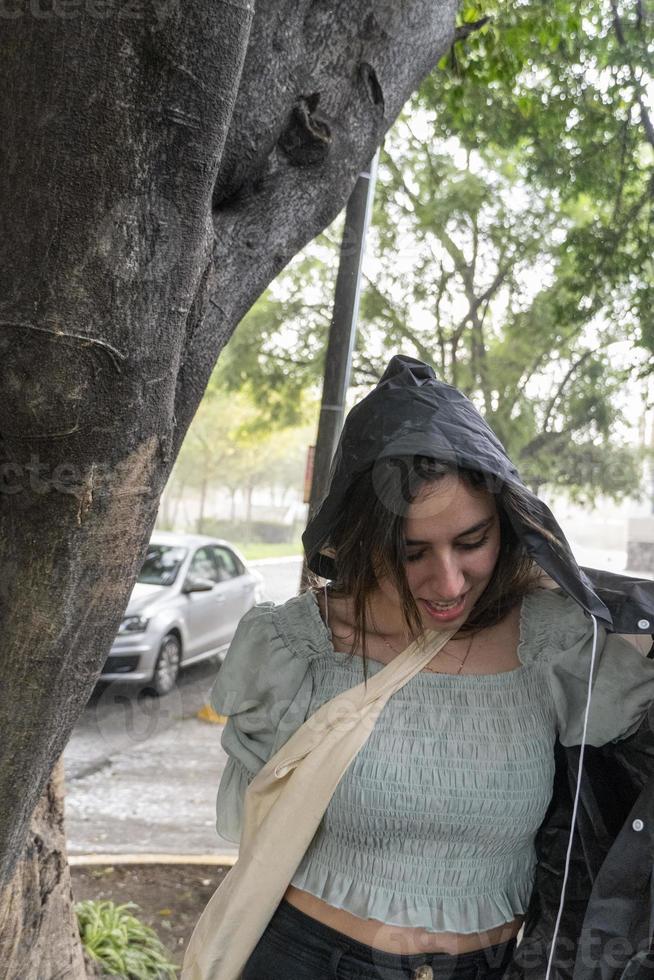 jovem vestindo capa de chuva em uma chuva inesperada repentina, abrigando-se em uma árvore, molhada, méxico foto