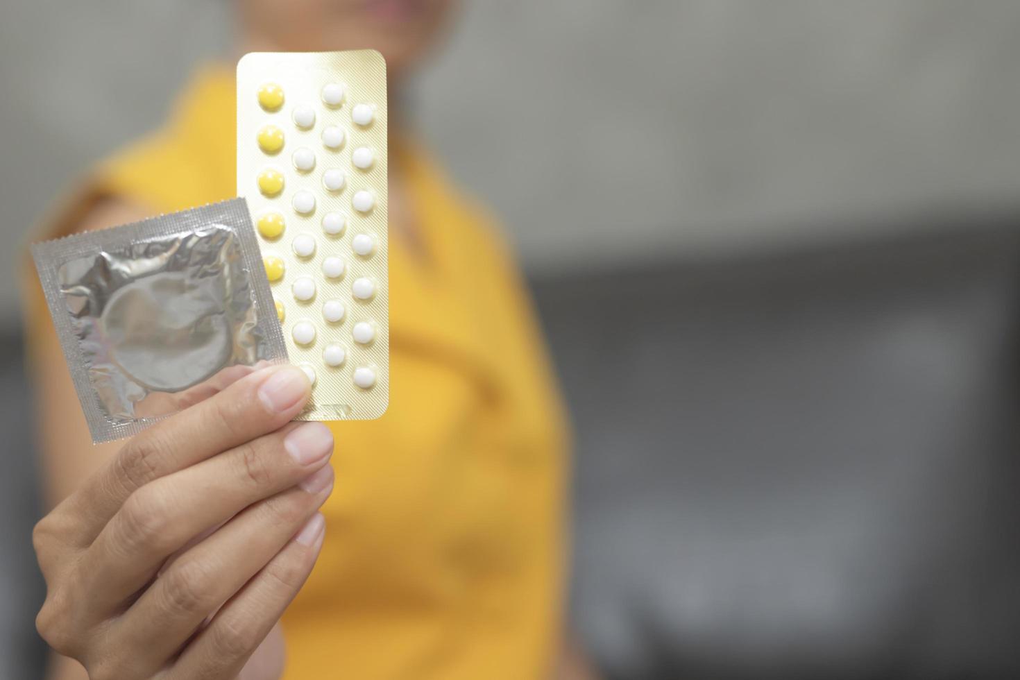 mulher segurando preservativo e pílulas anticoncepcionais foto