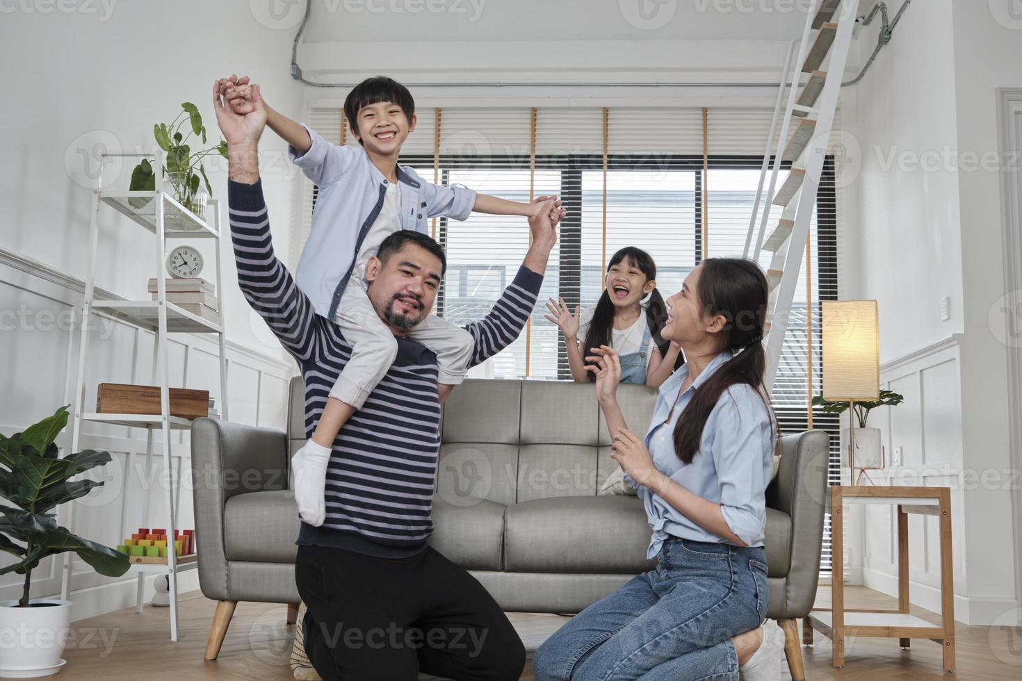 família tailandesa asiática junto, papai brinca e brinca com crianças e mamãe carregando e segurando o filho nos ombros na sala de estar em casa, momentos de lazer felizes, fim de semana adorável, estilo de vida doméstico de bem-estar. foto