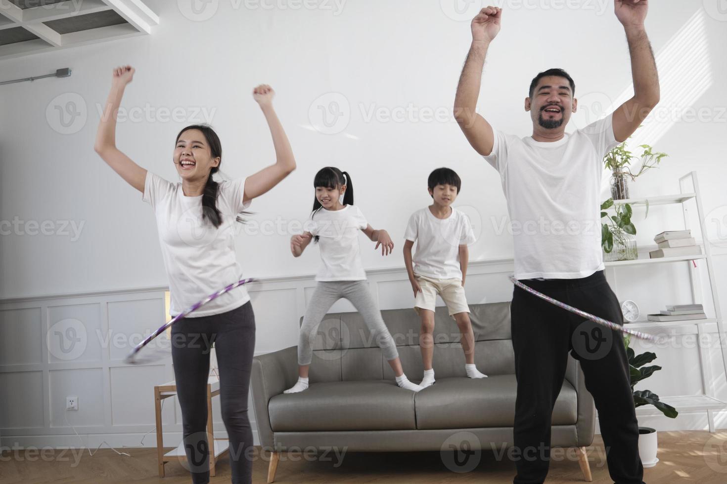 feliz bem-estar família tailandesa asiática, pais e filhos são divertidos jogando bambolê juntos, treinamento físico e exercícios saudáveis na sala de estar branca, estilo de vida doméstico e atividade de fim de semana. foto