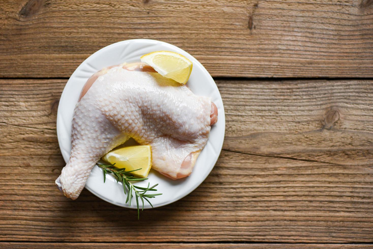 Coxa de frango crua no prato branco para cozinhar comida asiática tailandesa alecrim frango com limão na mesa de comida de madeira foto