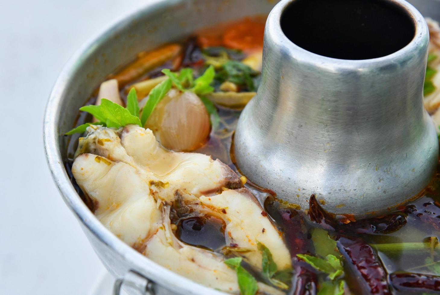 sopa de peixe quente e picante peixe tilápia cozido com ervas e especiarias na panela quente na mesa de jantar foto