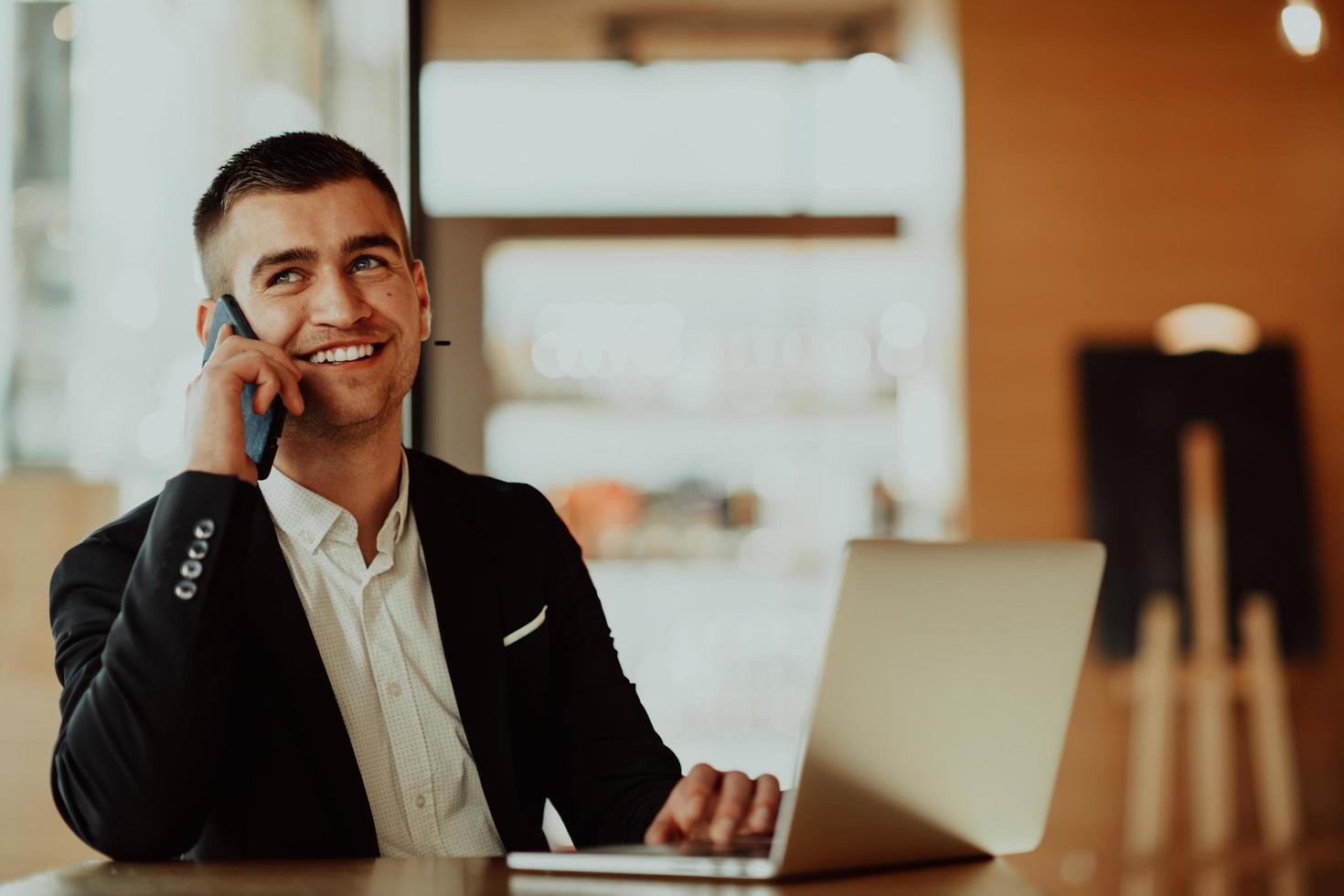 homem de negócios feliz sentado no refeitório com laptop e smartphone foto