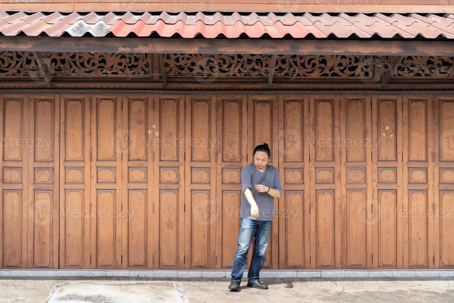 homem de cabelo comprido asiático está de pé e postando na frente da parede de madeira de fundo clássico e porta na frente do edifício tradicional vintage da tailândia. foto