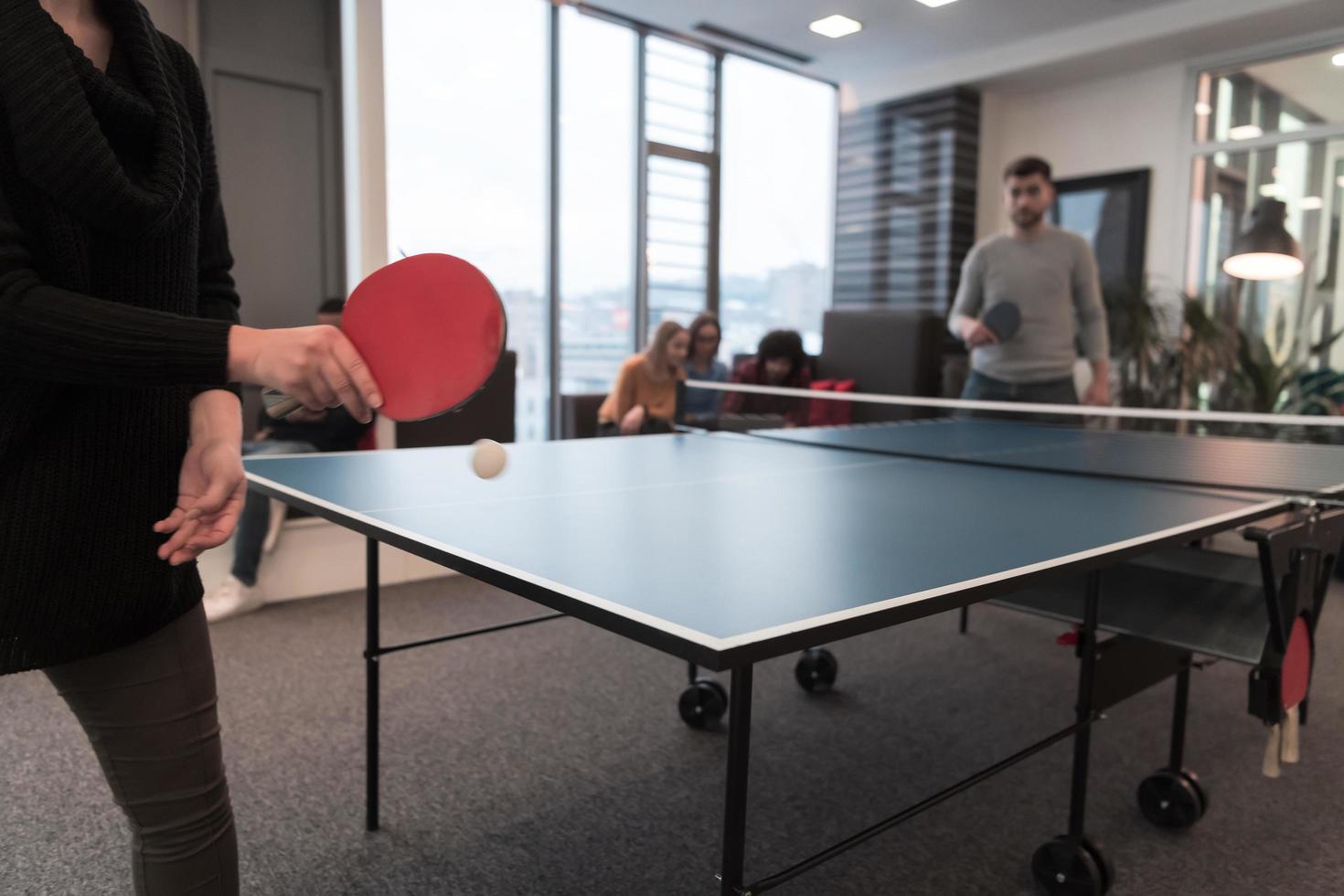 dois jovens iniciantes jogando tênis de mesa no moderno espaço de escritório criativo grupo de pessoas tem reunião e brainstorming em segundo plano foto