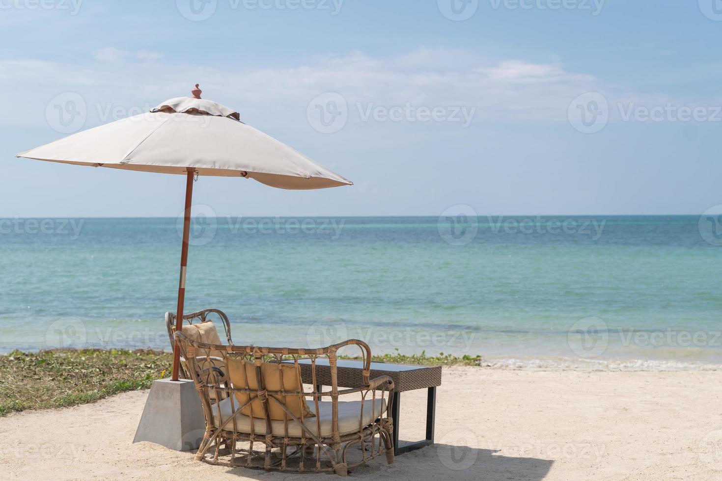 uma mesa com cadeiras e guarda-chuva para uma refeição romântica na praia, céu e mar ao fundo. foto