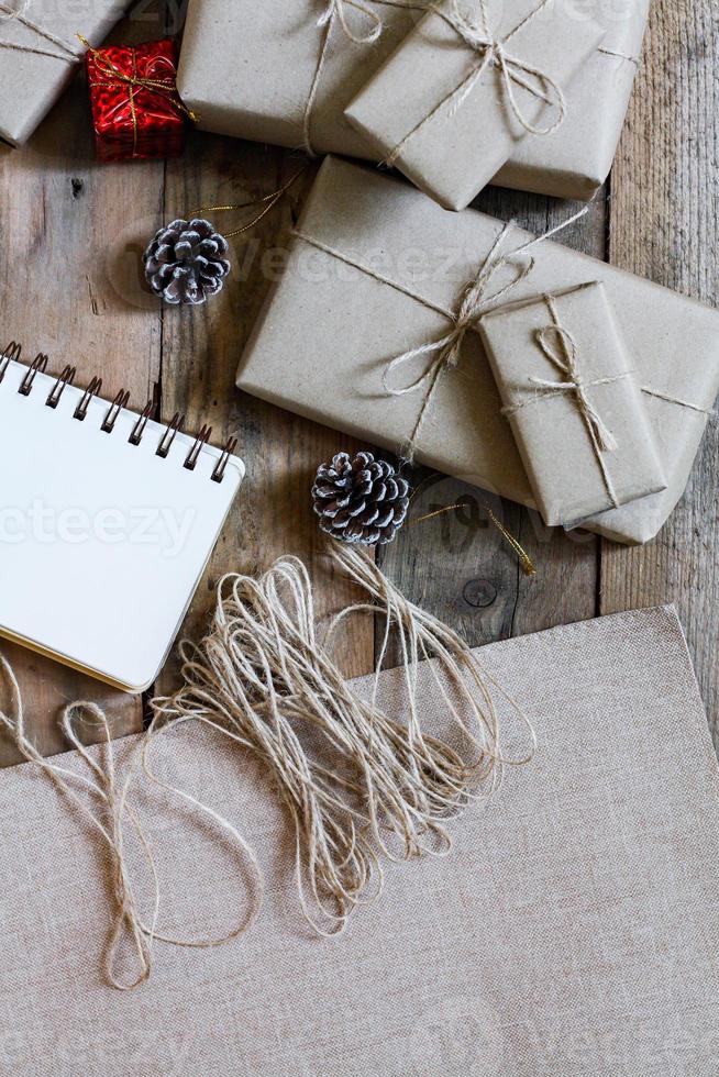 caixa de presente de natal usa papel reciclado marrom e um caderno e pinhas em uma mesa de madeira. foto