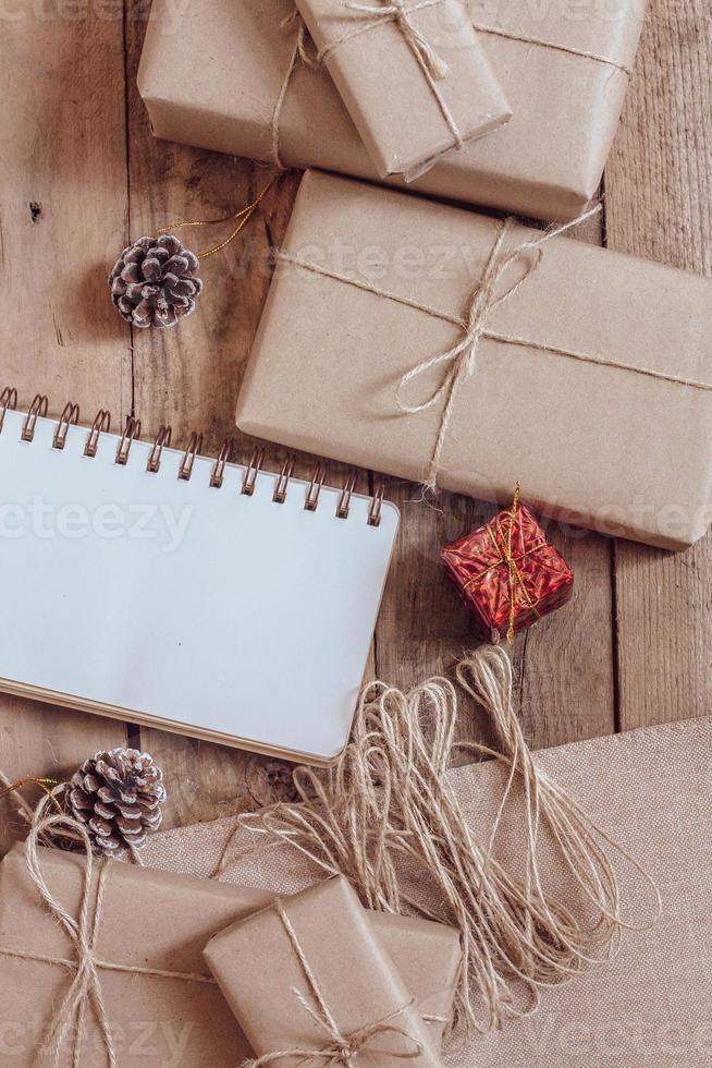 caixa de presente de natal usa papel reciclado marrom e um caderno e pinhas em uma mesa de madeira. foto