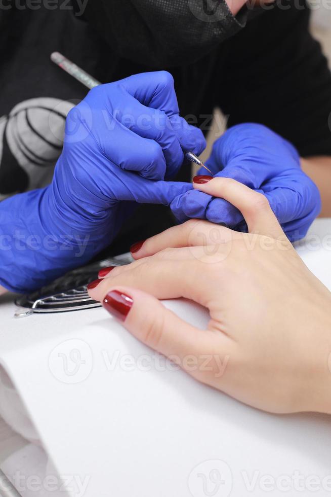 mestre em máscara protetora e luvas durante uma manicure no salão de beleza. mestre manicure enverniza o gel marsala nas unhas de uma cliente do sexo feminino. o conceito de beleza e saúde. foto