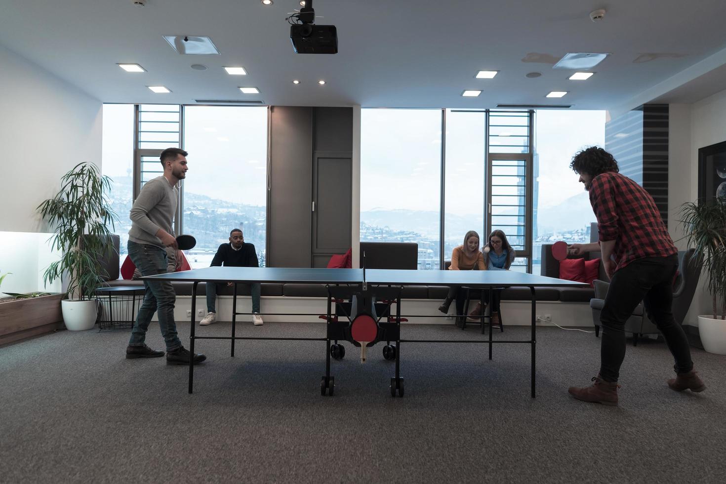 dois jovens iniciantes jogando tênis de mesa no moderno espaço de escritório criativo grupo de pessoas tem reunião e brainstorming em segundo plano foto