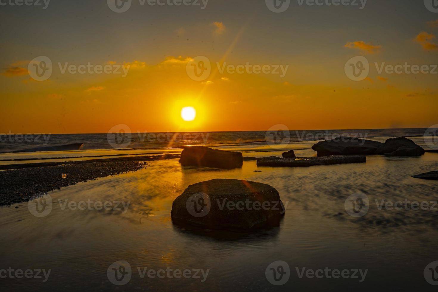 fotografia de longa exposição de ondas e seixos na praia por do sol foto