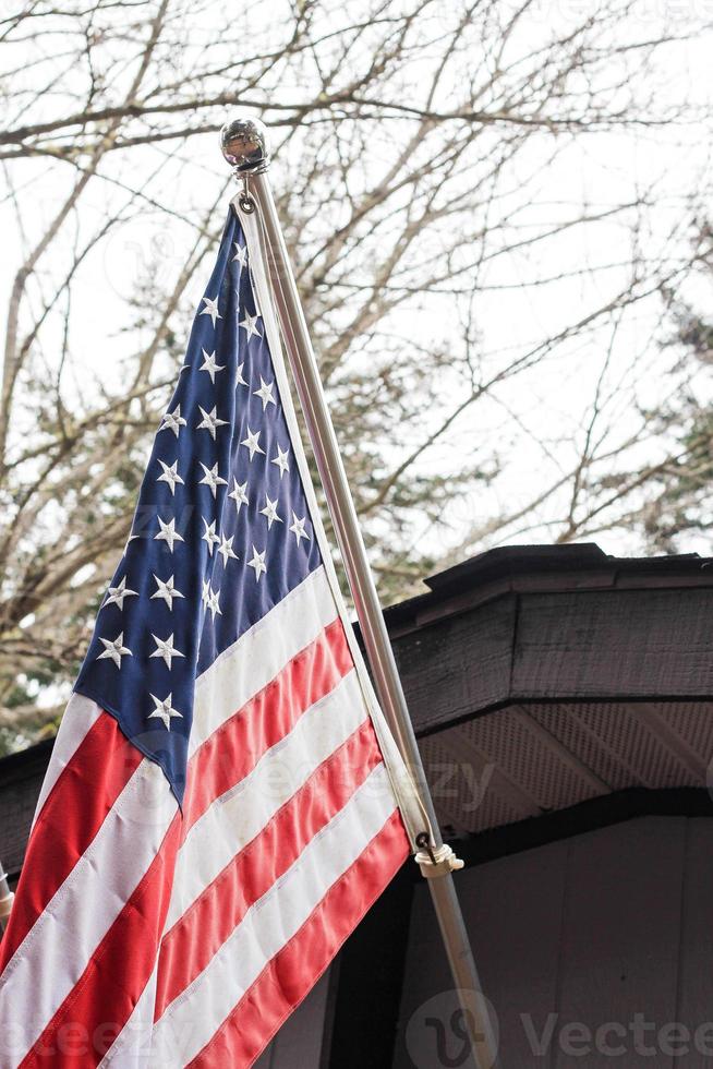 a bandeira americana na frente da casa contra o pano de fundo de uma árvore sem folhas no inverno. foto