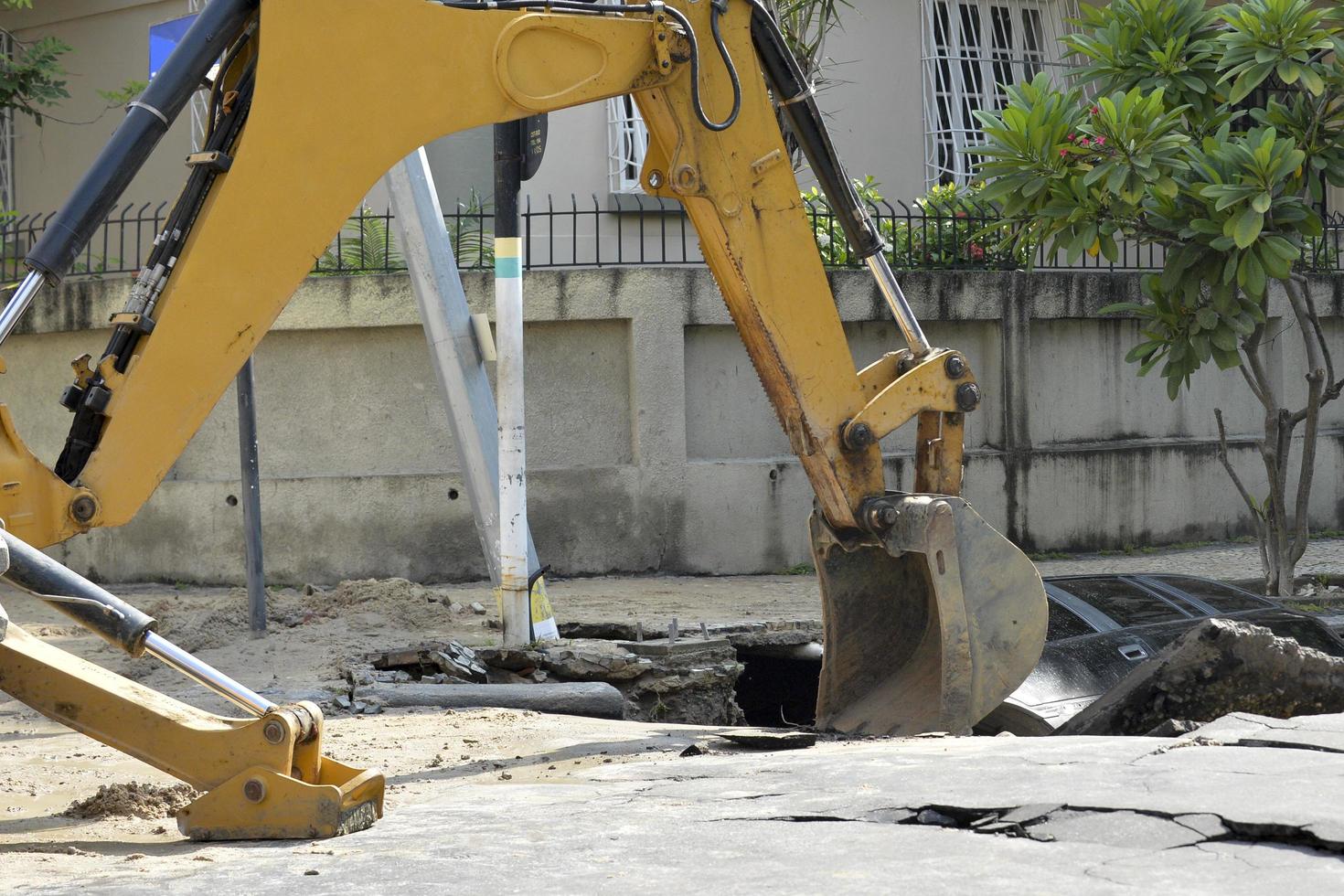 rio de janeiro, brasil - 02 de março de 2018 - retroescavadeira trabalha na remoção de um carro que caiu em um buraco, causado por vazamento de tubulação de água foto