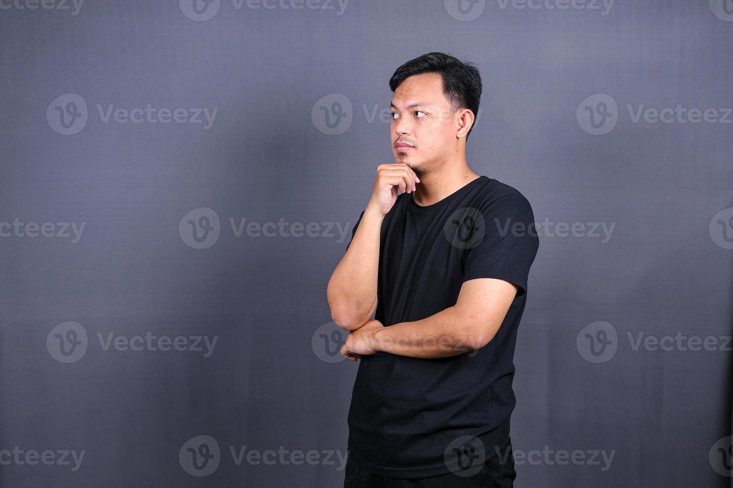 jovem asiático pensando em coisas ou ideia vestindo camiseta preta. fundo cinza isolado foto